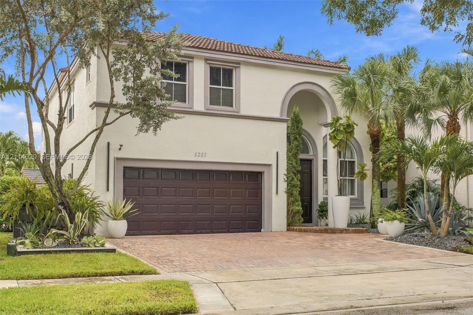 Stucco exterior featuring an arched entryway, terracotta-style roof tiles, a paver driveway, and a two-car garage
