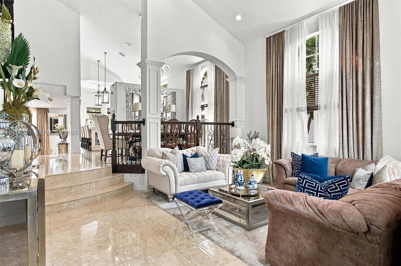 High-ceilinged living area featuring stone-finish tile flooring, arched architectural details, custom wrought-iron railings, and tall windows