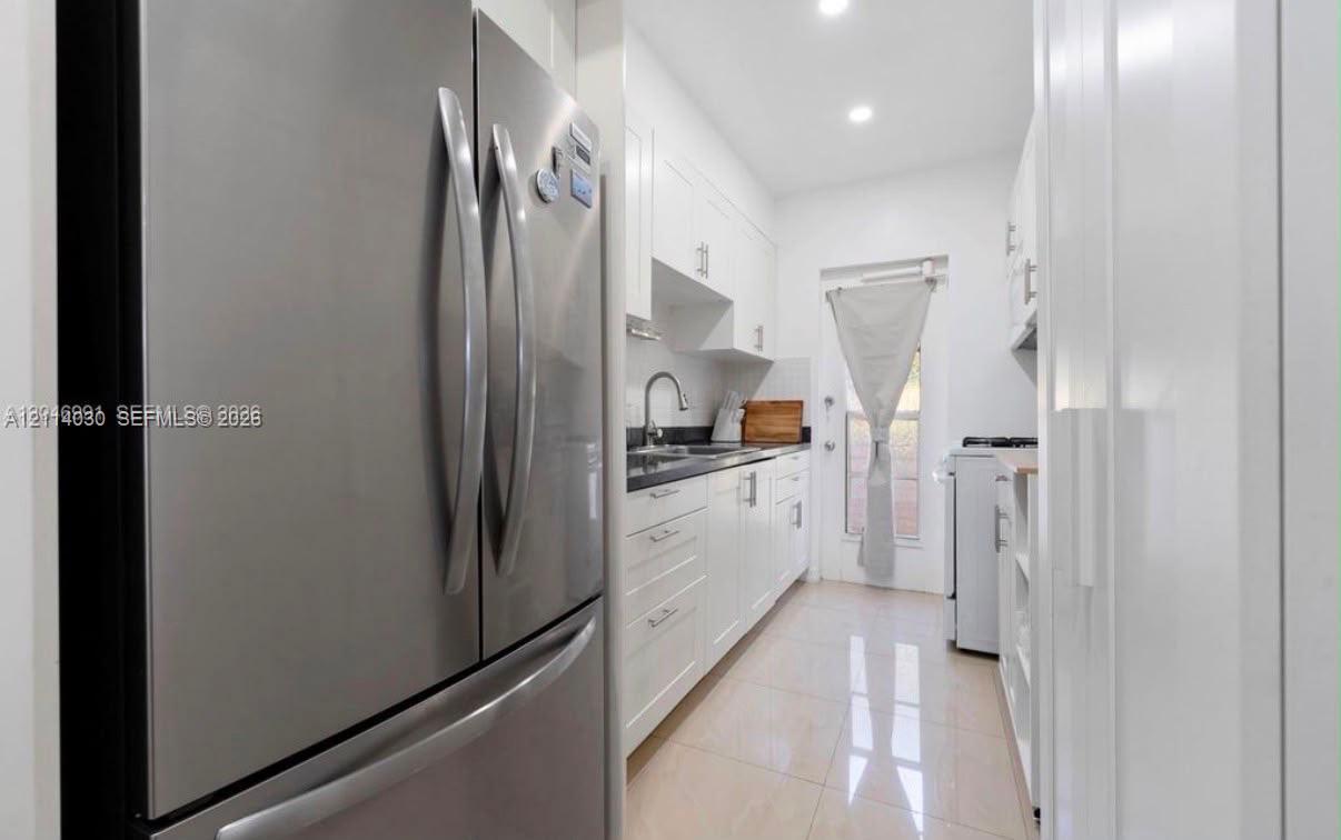 Kitchen featuring white shaker-style cabinetry, dark stone countertops, stainless steel refrigerator, recessed lighting, and tile flooring