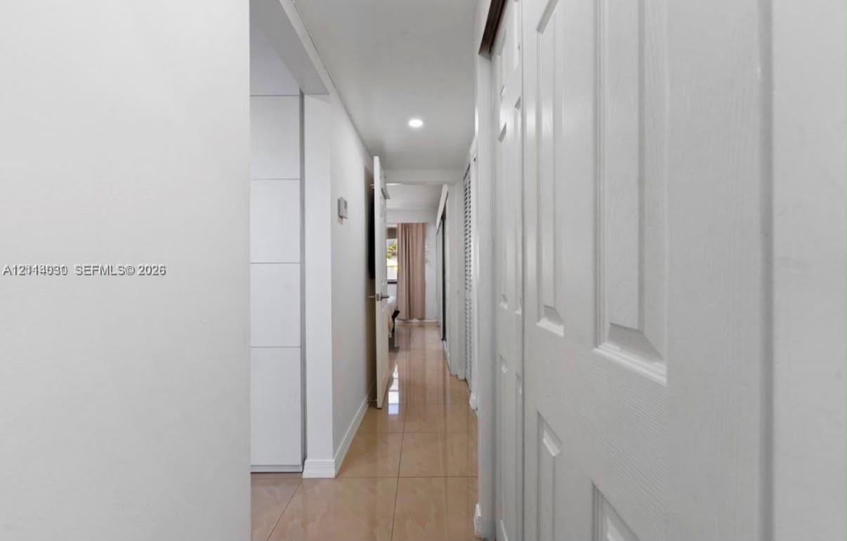 Hallway featuring light-toned tile flooring, recessed ceiling lighting, and floor-to-ceiling white built-in cabinetry with flush-panel doors