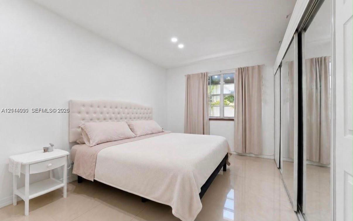 Bright room featuring neutral-toned tile flooring, recessed ceiling lighting, and floor-to-ceiling mirrored closet doors