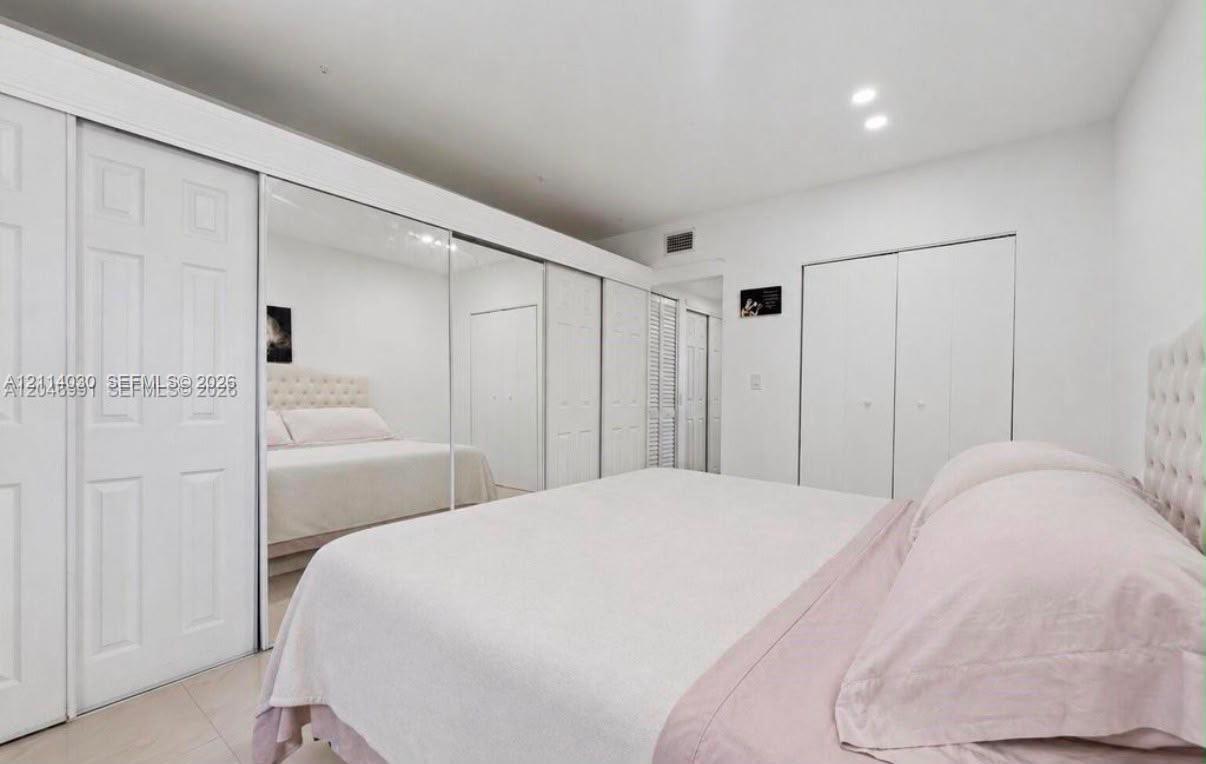 Full-wall mirrored sliding closet doors, expansive white cabinetry, and recessed lighting