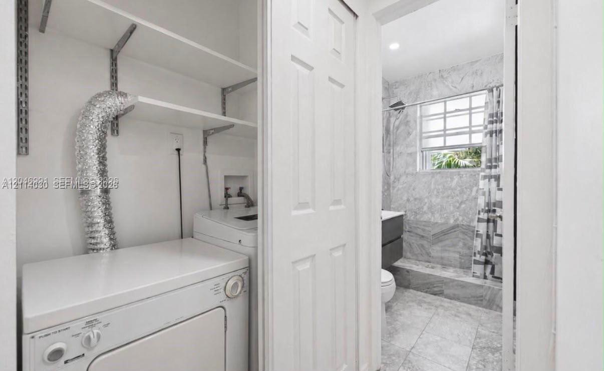 Laundry area featuring built-in white shelving, and bathroom equipped with stone-finish wall tile, tile flooring, and a window