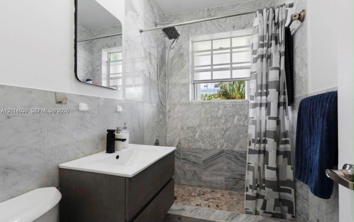Bathroom featuring floor-to-ceiling stone tile, floating vanity with integrated sink, matte black faucet, and rainfall shower head