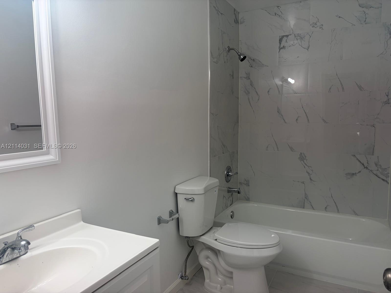 Bathroom featuring a vanity with an integrated sink, framed wall mirror, and a combination tub and shower enclosure with full-height stone-patterned tile surround Bathroom featuring a vanity with an integrated sink, framed wall mirror, and a combination tub and shower enclosure with full-height stone-patterned tile surround