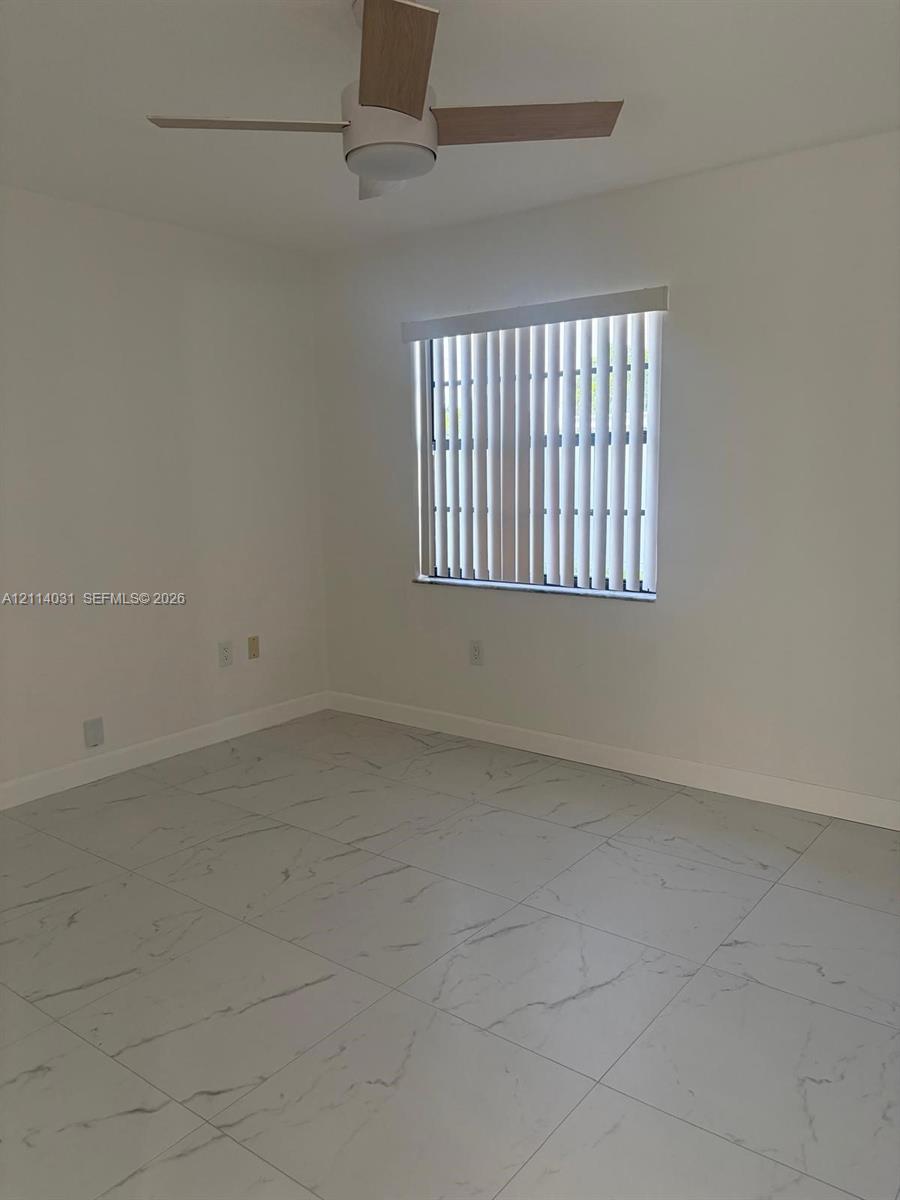 Room featuring large-format tile flooring with a neutral veined pattern, a ceiling fan, and a window with vertical blinds