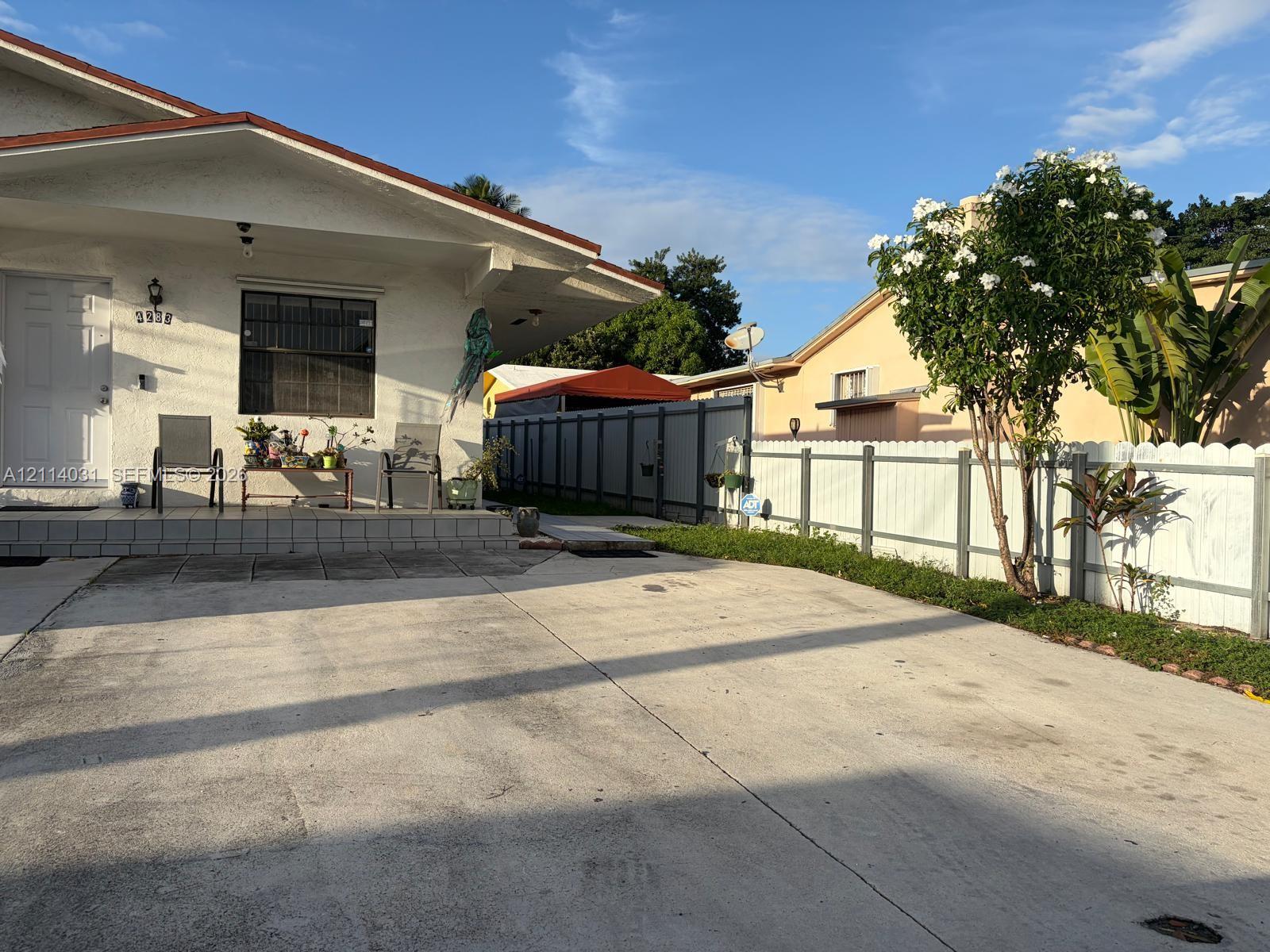 Stucco exterior residence featuring a tiled front porch, concrete driveway, and white picket-style fencing Stucco exterior residence featuring a tiled front porch, concrete driveway, and white picket-style fencing