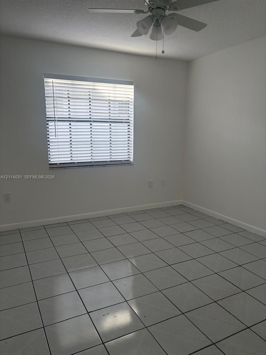 Room featuring neutral wall-to-wall ceramic tile flooring, a window with horizontal blinds, and a ceiling-mounted light fixture with a fan Room featuring neutral wall-to-wall ceramic tile flooring, a window with horizontal blinds, and a ceiling-mounted light fixture with a fan