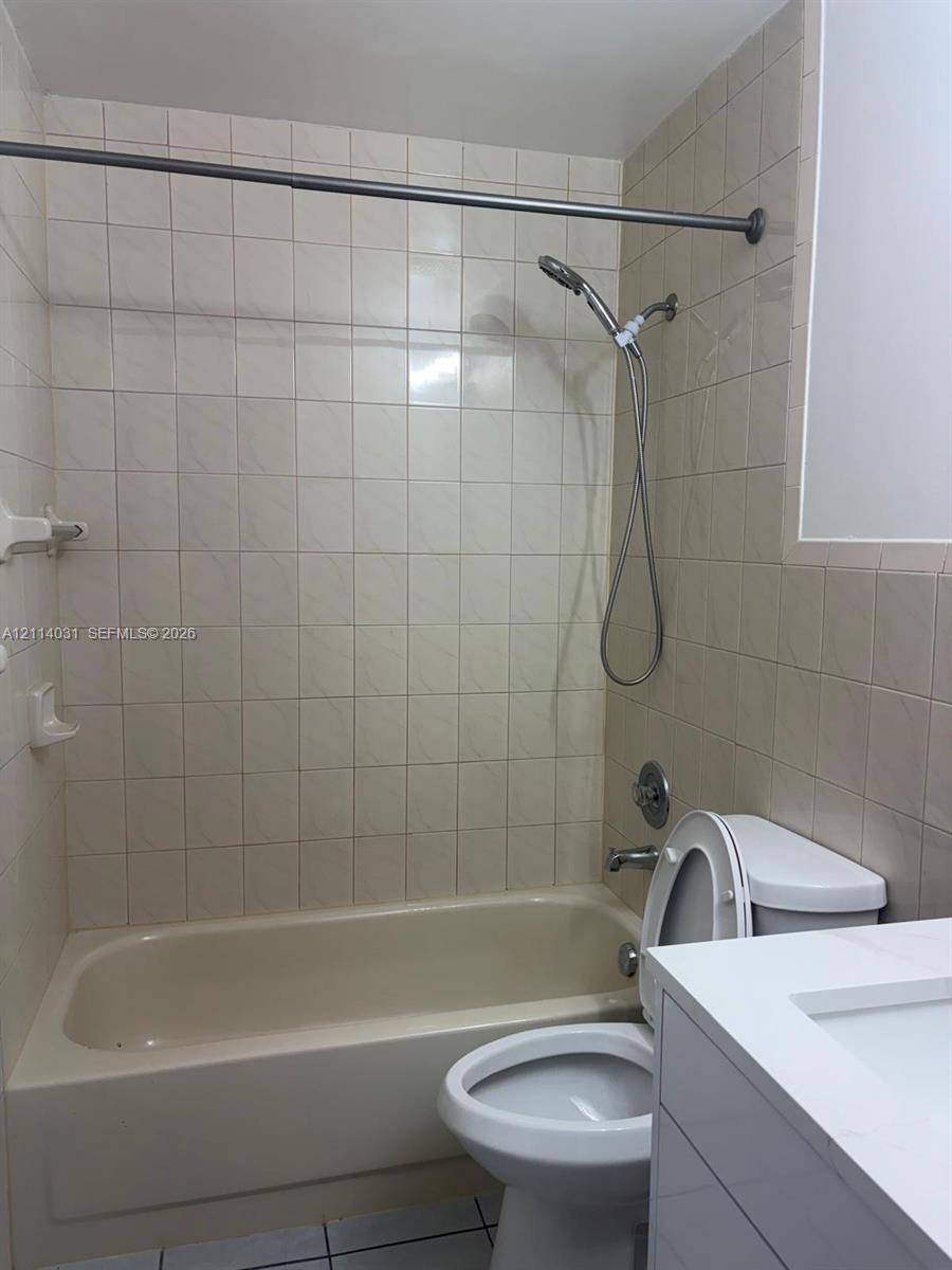 Full bathroom featuring a tub-shower combination with square wall tile, a hand-held shower fixture, a vanity with a white countertop and integrated sink, and tile flooring Full bathroom featuring a tub-shower combination with square wall tile, a hand-held shower fixture, a vanity with a white countertop and integrated sink, and tile flooring