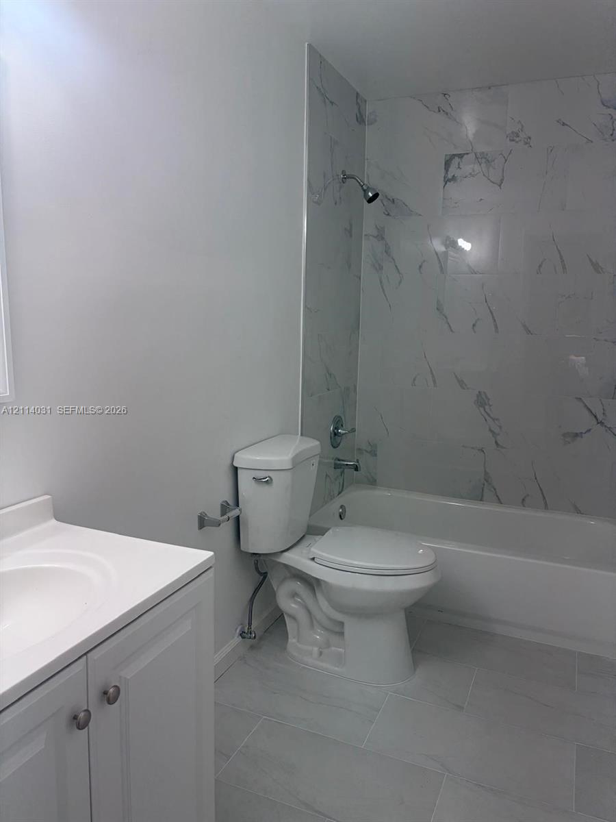 Bathroom featuring large-format tile flooring, vanity with integrated basin, and full-height tiled tub surround