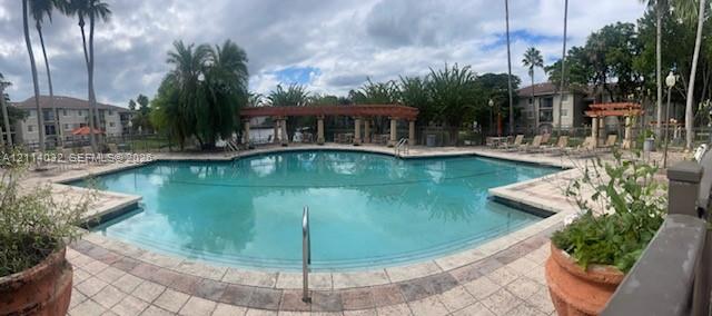 Swimming pool with a paved deck, built-in wooden pergola, and mature landscaping