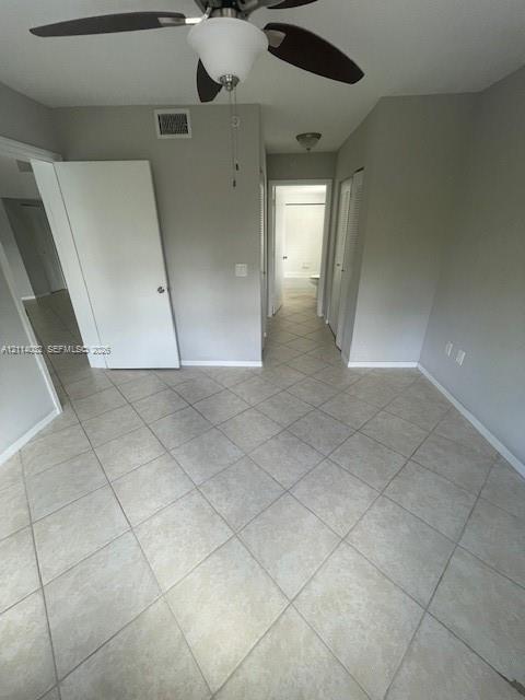 Neutral-toned interior space featuring light-colored diagonal floor tiling, a ceiling fan with integrated lighting, and multiple interior doorways