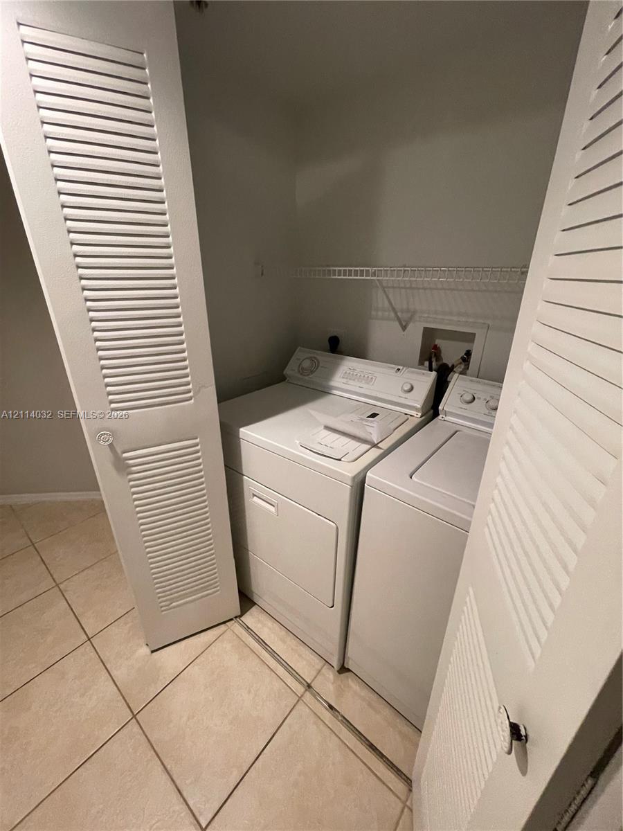 Laundry closet featuring white louvered doors, tile flooring, and integrated wire shelving