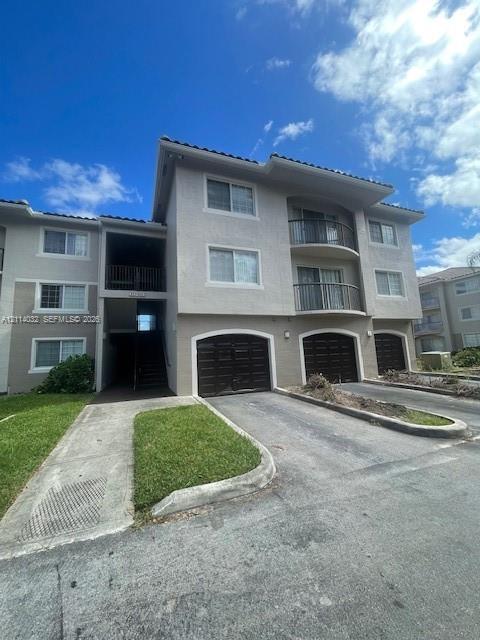 Multi-story exterior featuring a stucco facade, private garage bays with arched detailing, and stacked balconies with metal railings Multi-story exterior featuring a stucco facade, private garage bays with arched detailing, and stacked balconies with metal railings