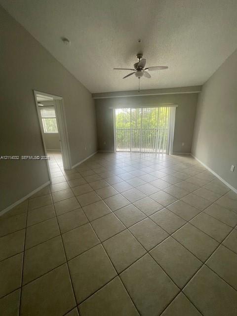 Vaulted ceilings, neutral tile flooring, ceiling fan with light fixture, and floor-to-ceiling sliding glass doors