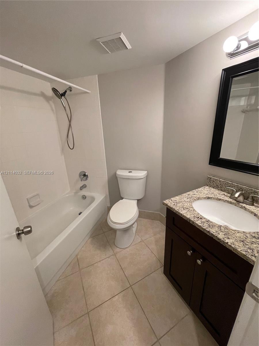 Bathroom featuring a dark wood vanity with a stone countertop, an integrated porcelain sink, tile flooring, and a shower-tub combination