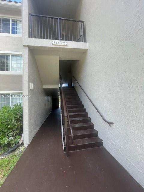 Exterior entrance featuring a stucco facade, dark-toned stairs, and a metal handrail