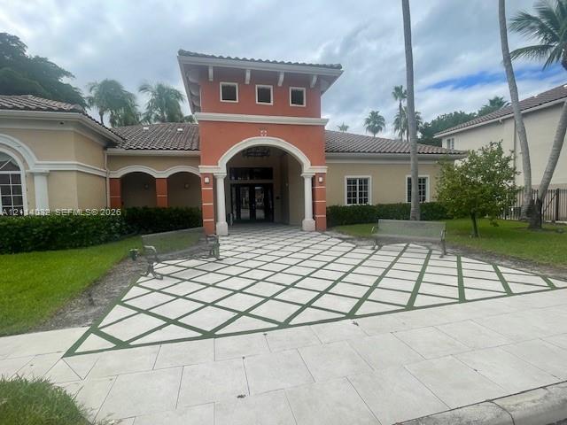 Mediterranean-inspired exterior featuring a stucco facade, central arched entryway, decorative diamond-patterned paved courtyard, and tiled hip roof