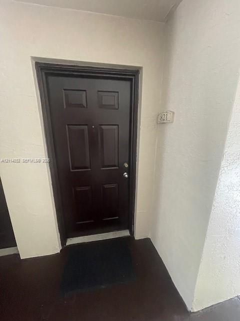 Six-panel dark-finish entry door with a door viewer and metallic hardware, complemented by a textured neutral-toned surround and unit number plaque