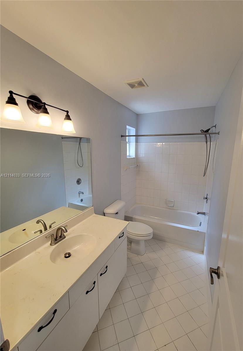 Bathroom featuring a white vanity with a solid surface countertop, an oval undermount sink, a three-light fixture, and a tub-shower combination with ceramic tile surround