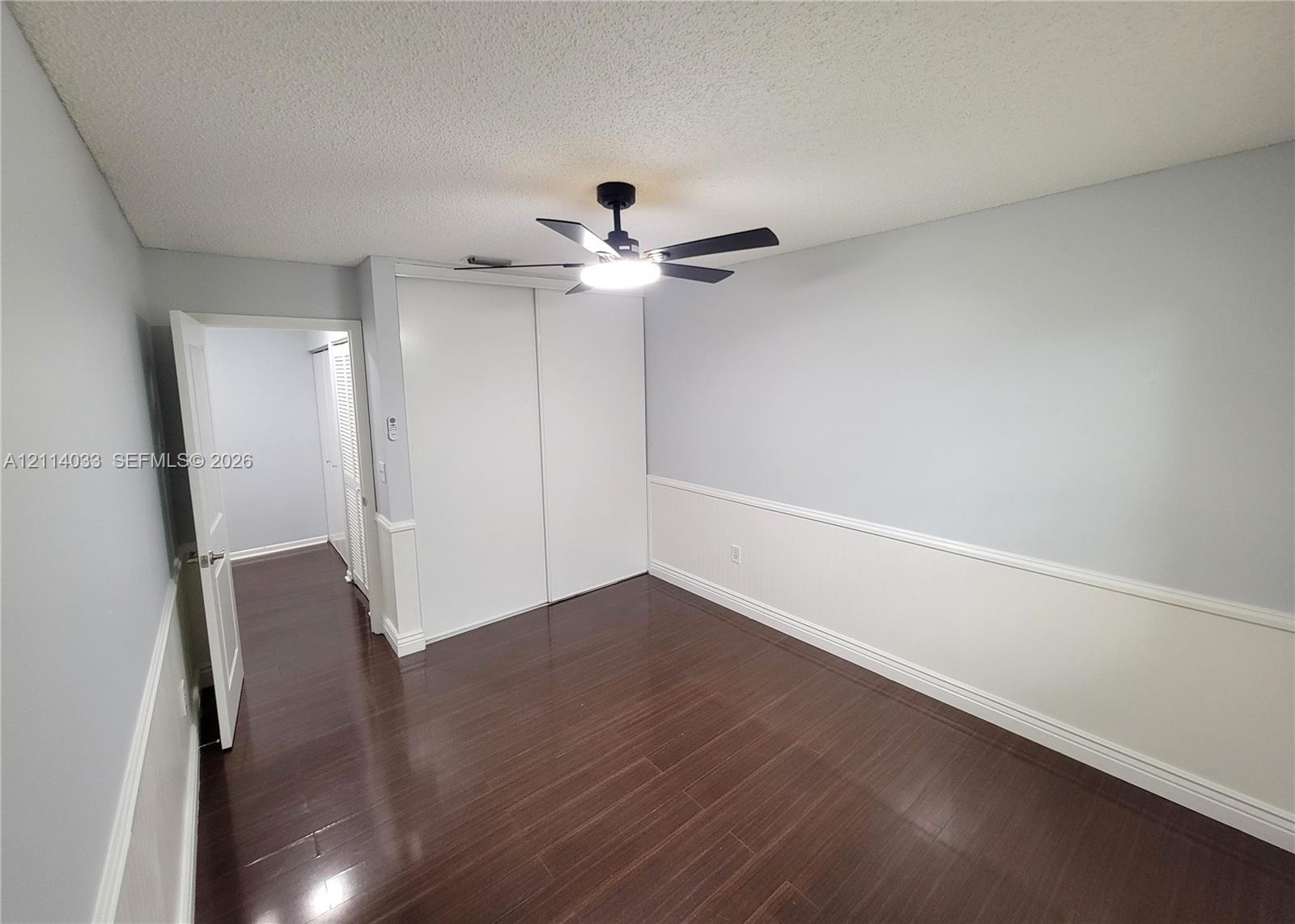 Interior room featuring dark wood-finish flooring, two-tone walls with chair rail molding, a sliding-door closet, and an attached ceiling fan with integrated lighting