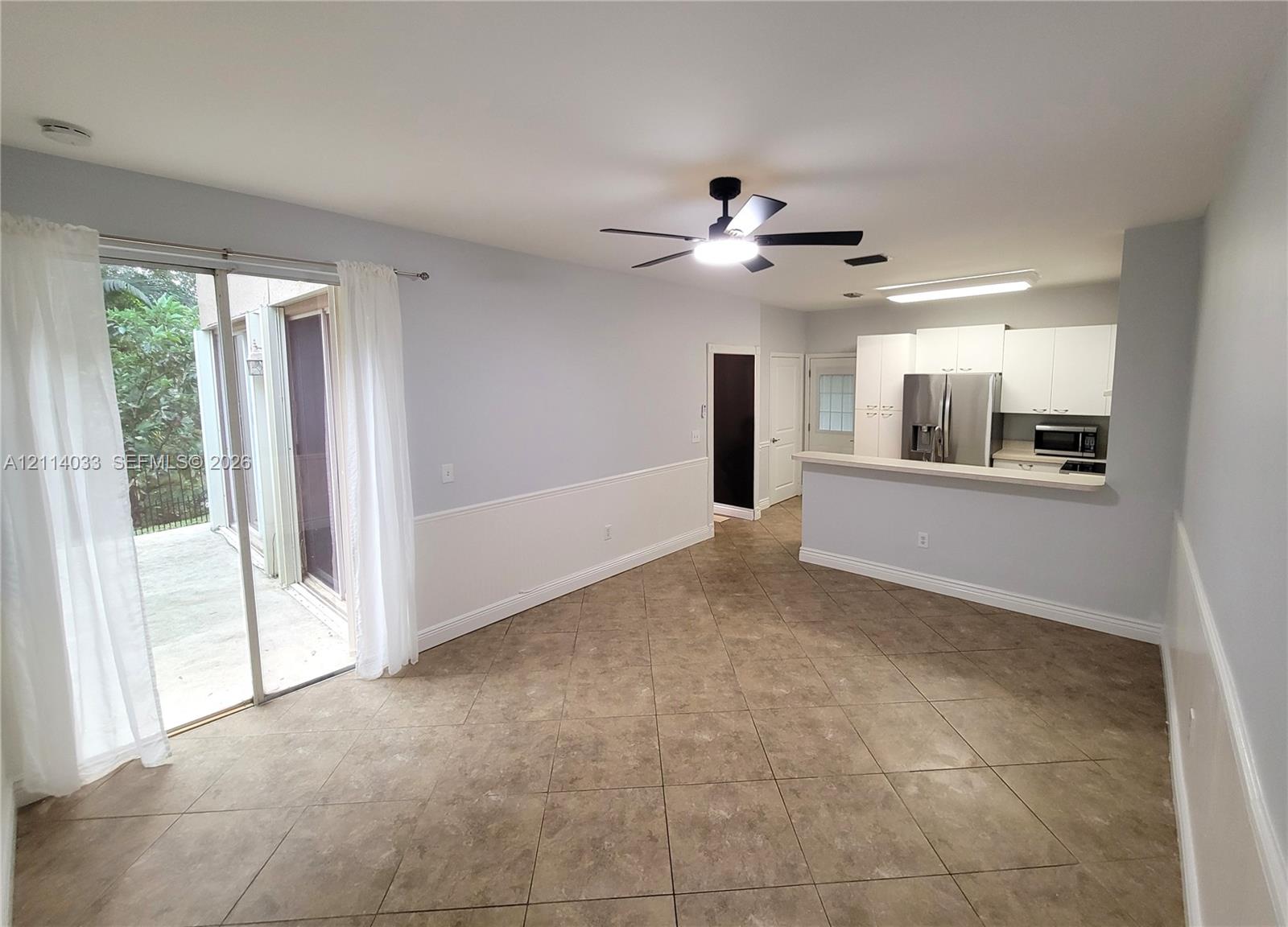 Large-format tile flooring, kitchen with white cabinetry and stainless steel appliances, breakfast bar, ceiling fan, and sliding glass doors