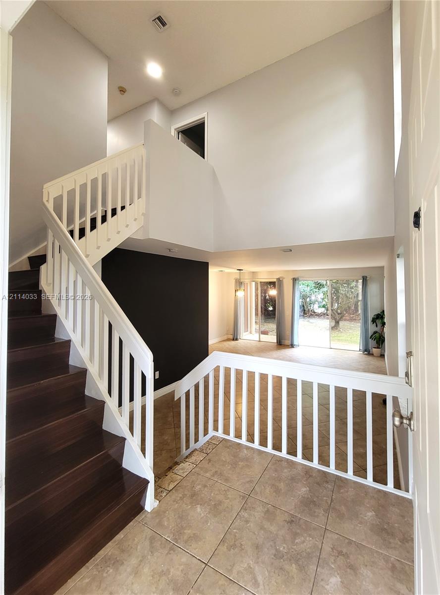 Foyer featuring high ceilings, wood-finish staircase treads, white balustrades, large-format tile flooring, and sliding glass doors