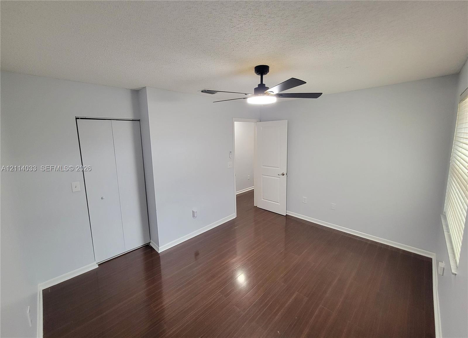 Room featuring dark wood-finish flooring, a matte black ceiling fan with an integrated light fixture, a bi-fold closet, and a white interior door