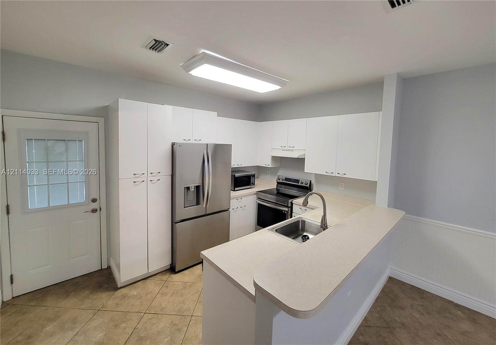 Kitchen featuring white cabinetry, stainless steel appliances, a peninsula with a stainless steel sink, and tile flooring