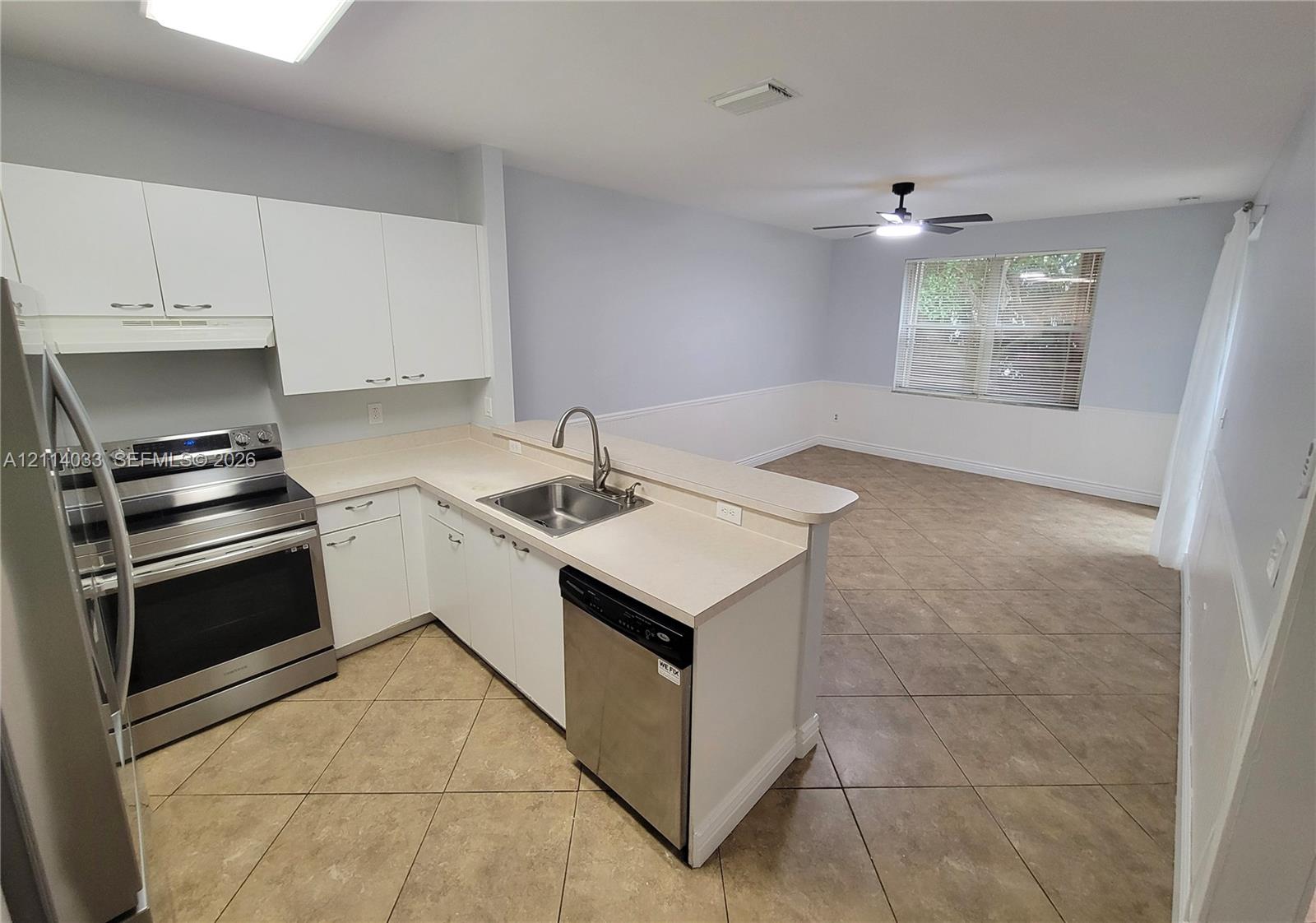 Kitchen featuring white cabinetry, neutral-toned countertops, stainless steel appliances, a double-basin undermount sink with a gooseneck faucet, and tile flooring