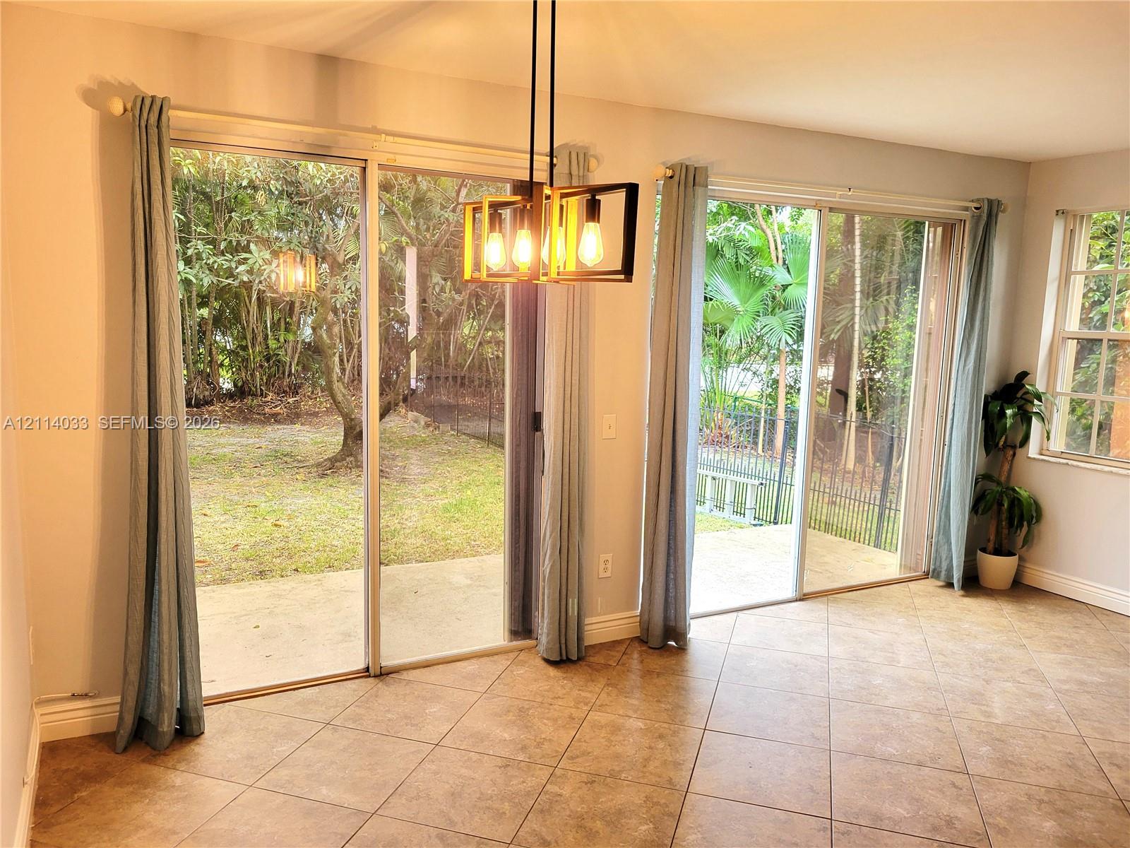 Dual glass sliding doors, ceramic tile flooring, geometric metal pendant lighting, and access to a concrete patio