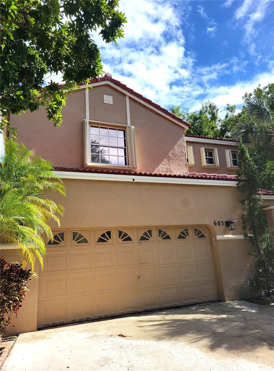 Stucco exterior featuring a dual-pitch tile roof, arched-top garage door panels, and decorative trim shutters Stucco exterior featuring a dual-pitch tile roof, arched-top garage door panels, and decorative trim shutters