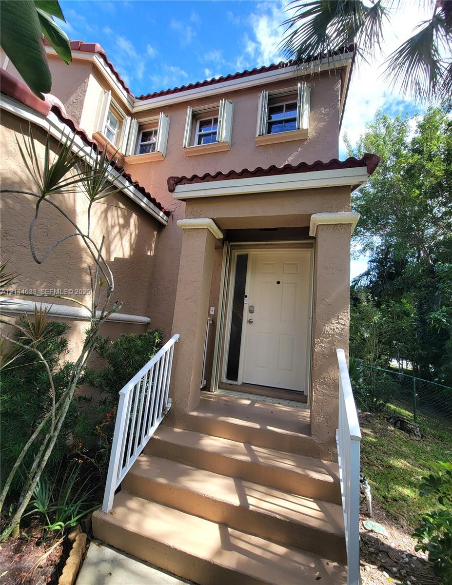 Stucco exterior featuring a tiled roofline, covered entryway, and white metal railings