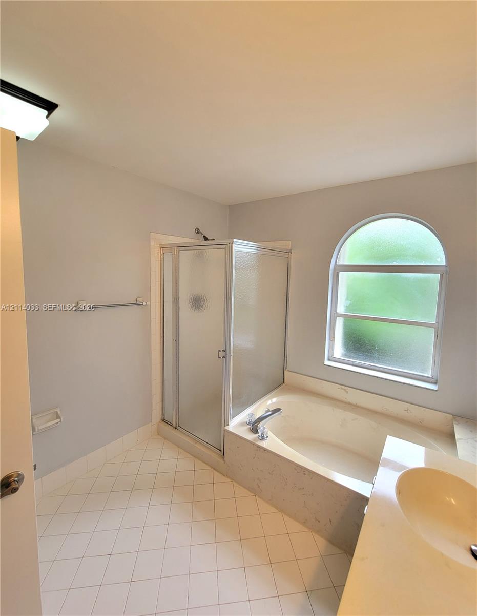 Bathroom featuring a soaking tub, separate glass-enclosed shower, arched window, and tile flooring