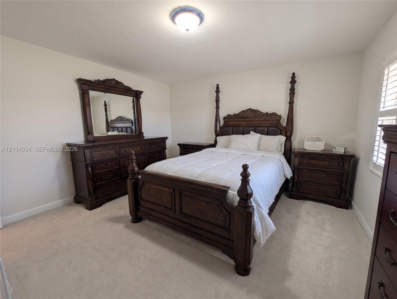 Second bedroom with neutral-toned wall paint, plush carpeting, and plantation-style window shutters
