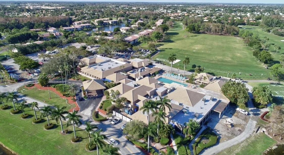 Aerial perspective featuring a multi-wing complex with pitched rooflines, an outdoor swimming pool, and extensive grounds with mature palm trees