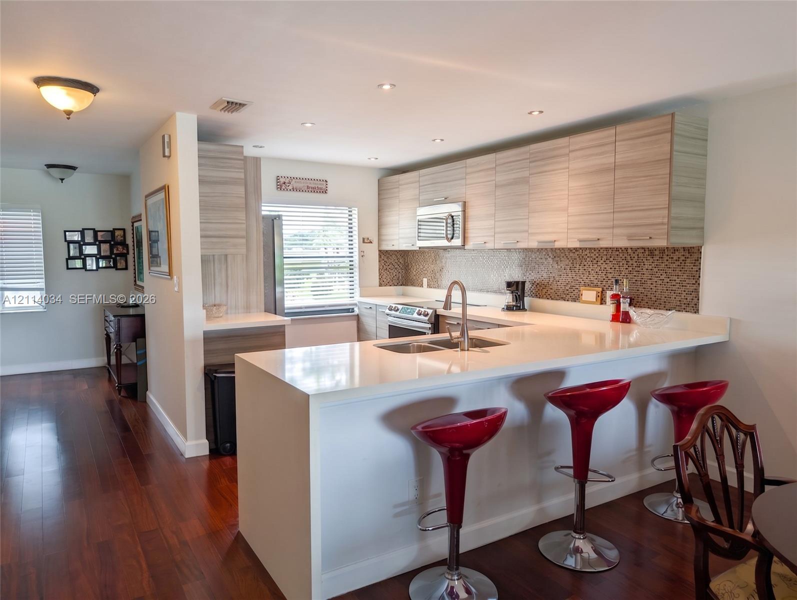 Kitchen featuring wood-finish cabinetry, quartz countertops, mosaic tile backsplash, stainless steel appliances, and wood-finish flooring Kitchen featuring wood-finish cabinetry, quartz countertops, mosaic tile backsplash, stainless steel appliances, and wood-finish flooring