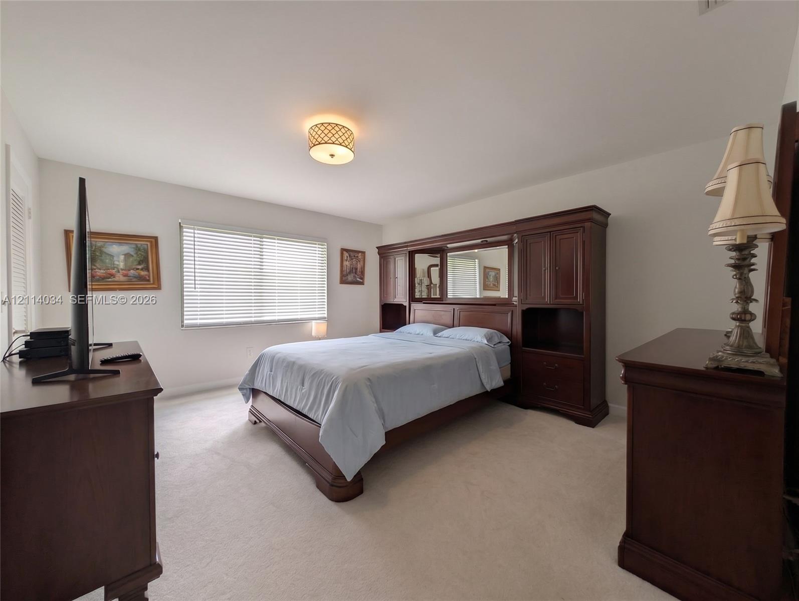 Master bedroom featuring neutral carpeting, horizontal window blinds, and a circular drum-style ceiling light fixture