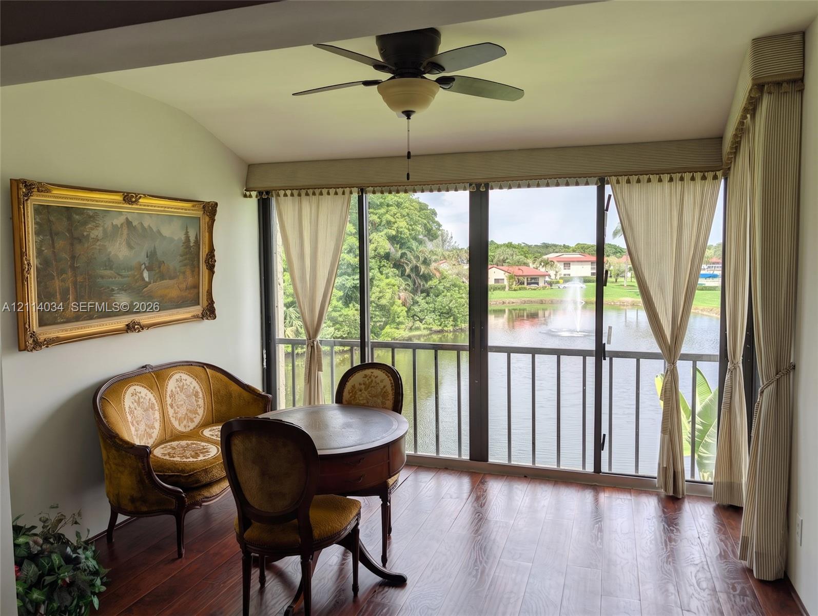 Floor-to-ceiling windows featuring a metal railing, rich wood-finish flooring, and a ceiling-mounted light fixture with a multi-blade fan