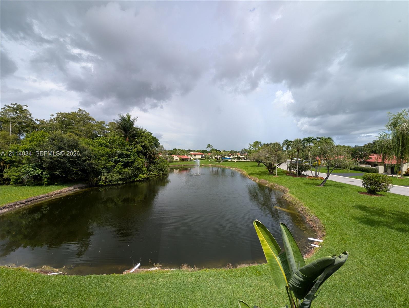 Waterfront parcel featuring a central pond, an aerating fountain, mature perimeter landscaping, and expansive green space