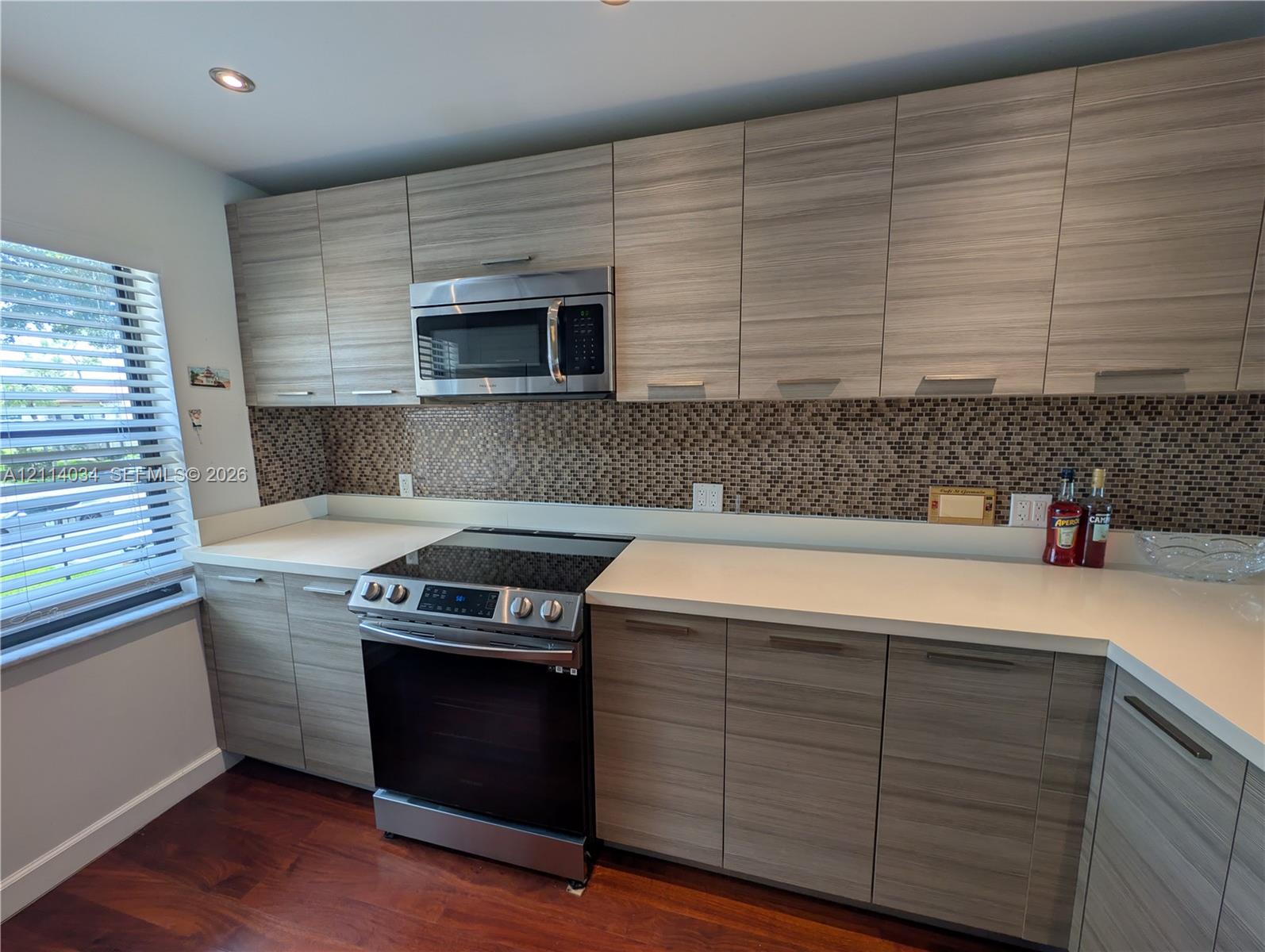 Kitchen featuring horizontal wood-grain cabinetry, stainless steel appliances, solid surface countertops, and a decorative pebble-tile backsplash