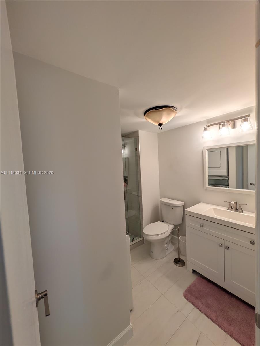 Bathroom featuring a white vanity cabinet with a rectangular basin, ceramic tile flooring, a glass-enclosed shower, and a wall-mounted multi-light fixture