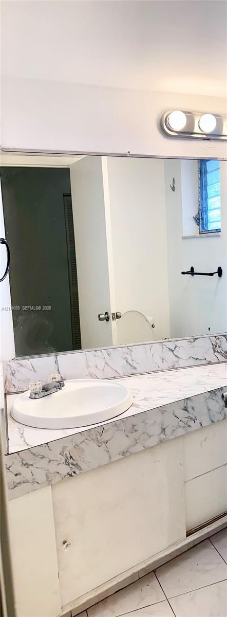 Bathroom vanity featuring a stone-patterned countertop, an integrated sink with dual-handle faucet, full-width wall mirror, and dual-bulb vanity light fixture