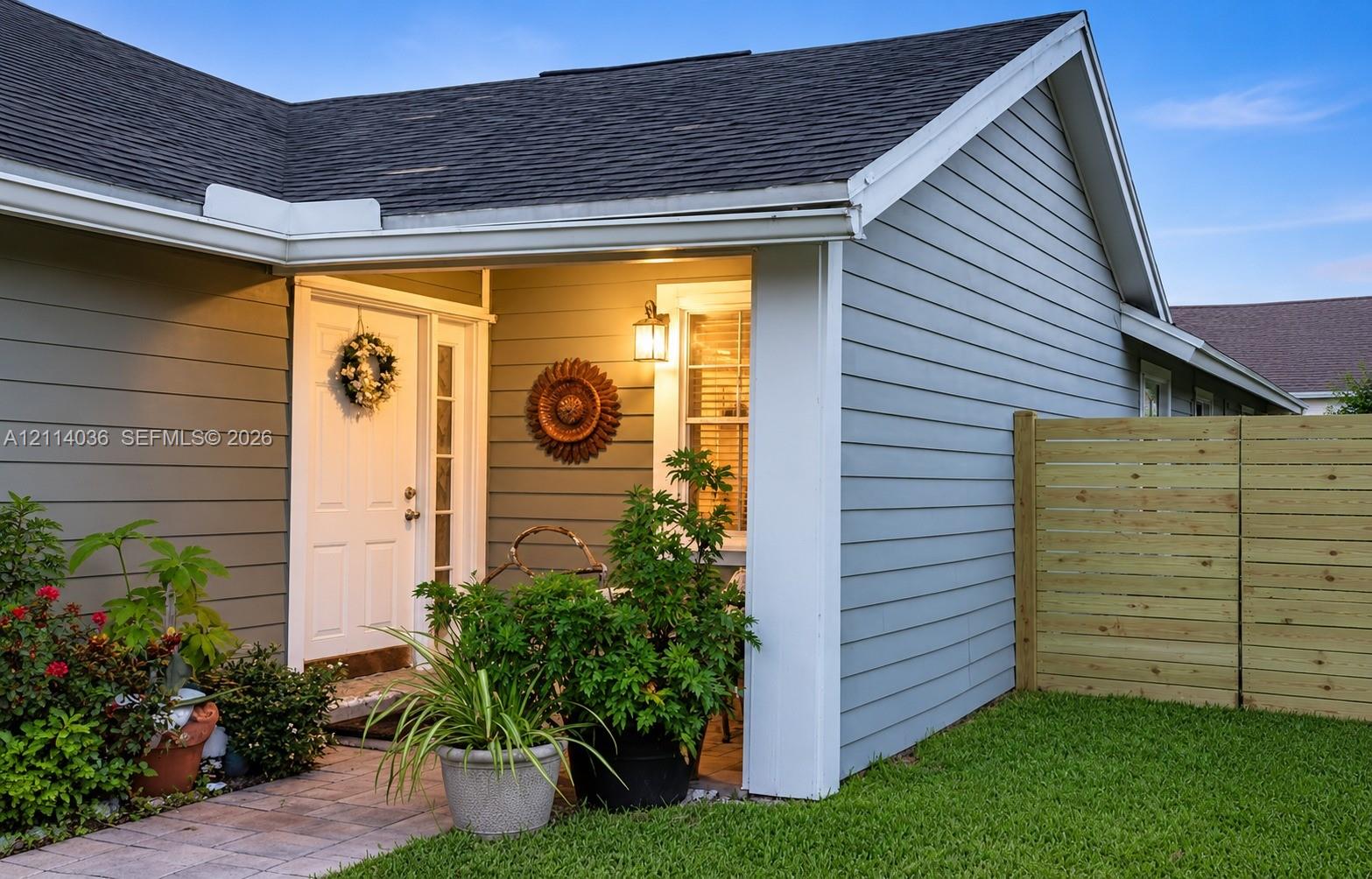 Covered entryway featuring horizontal lap siding, a paneled door with glass sidelight, exterior wall-mounted lighting, and a stone-paver walkway