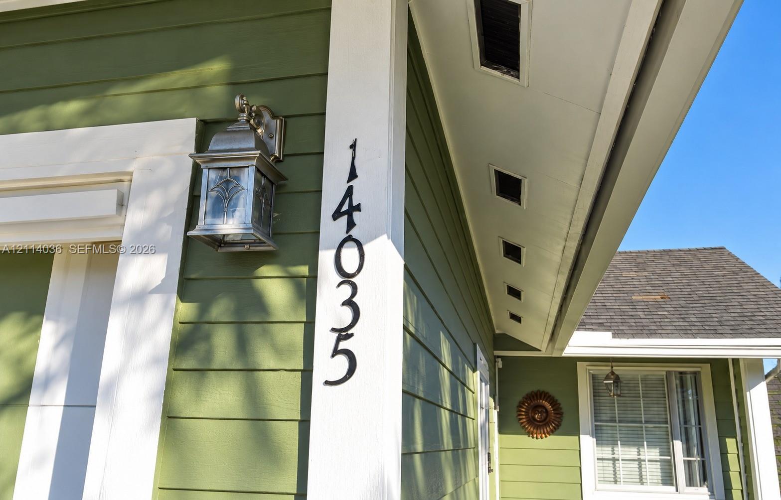 Exterior elevation featuring sage green horizontal lap siding, white trim, custom metal wall-mounted lantern, and high-contrast vertical house numbering