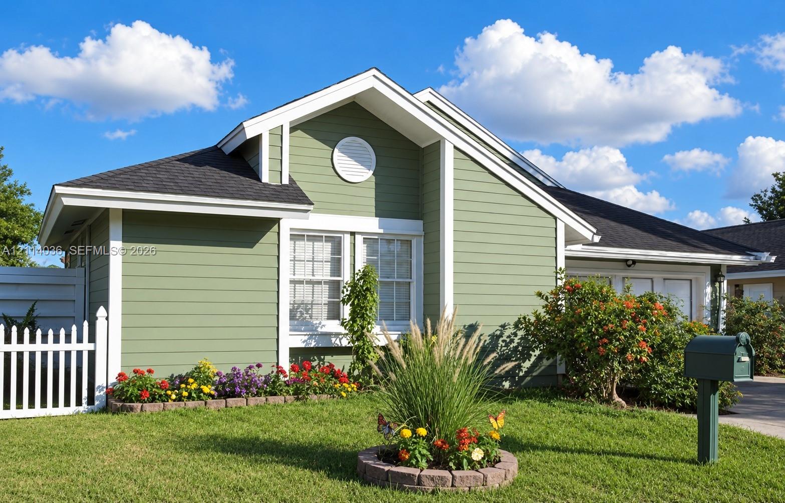 Single-story residence featuring horizontal lap siding, a gabled roofline, a white picket fence, and a circular stone-lined garden bed