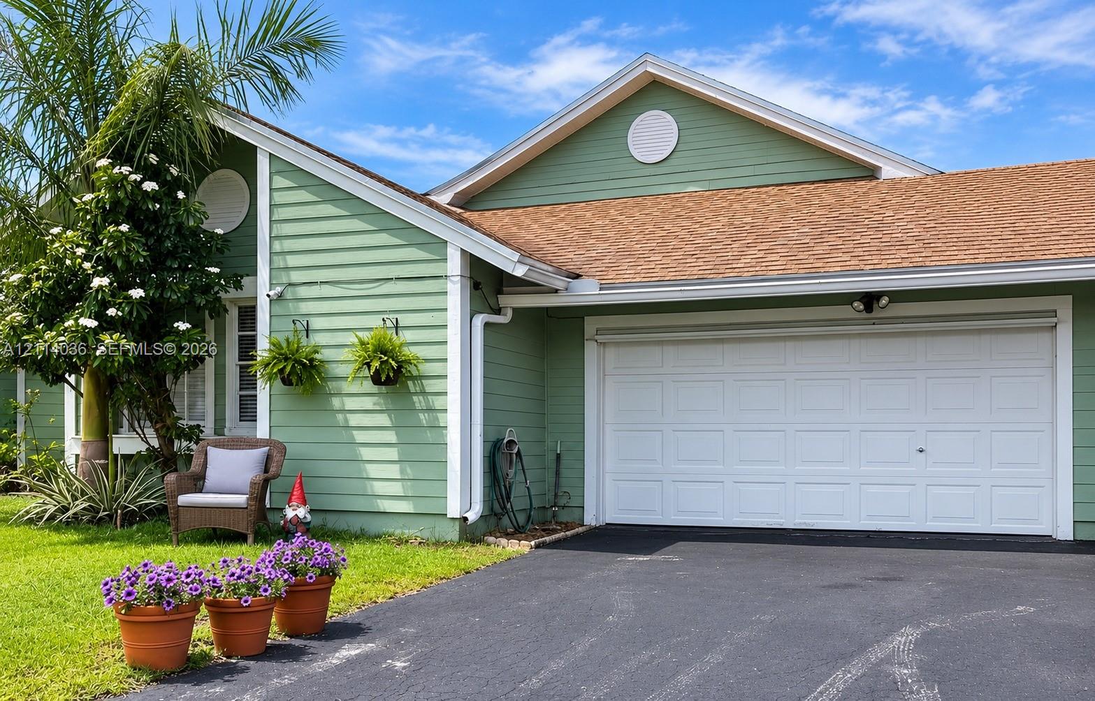 Exterior featuring horizontal lap siding, shingle roof, attached garage with white paneled door, circular gable vents, and paved driveway