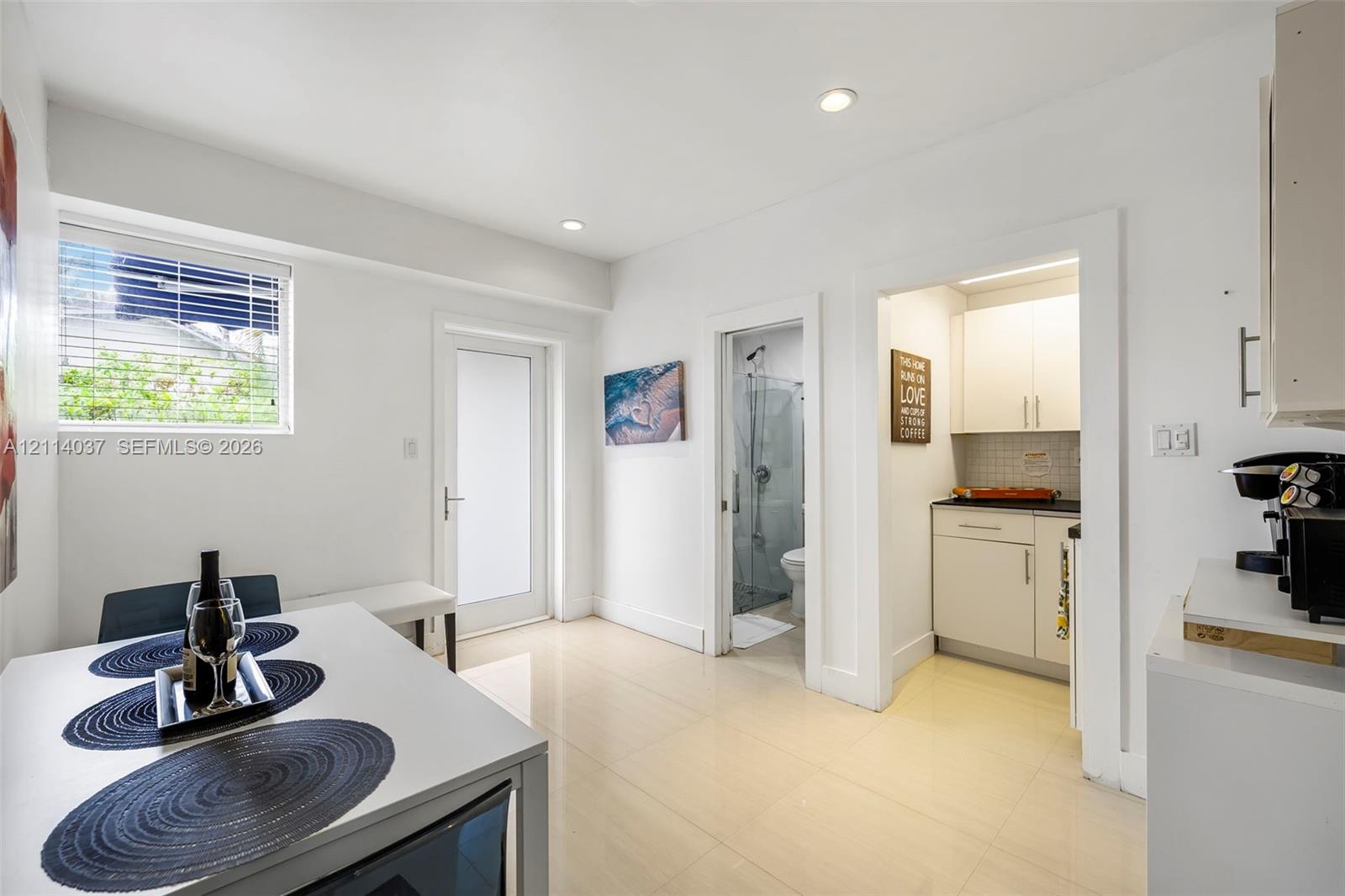 Neutral-toned tile flooring, recessed ceiling lighting, glass-panel entry door, and white cabinetry with a dark stone-surface countertop