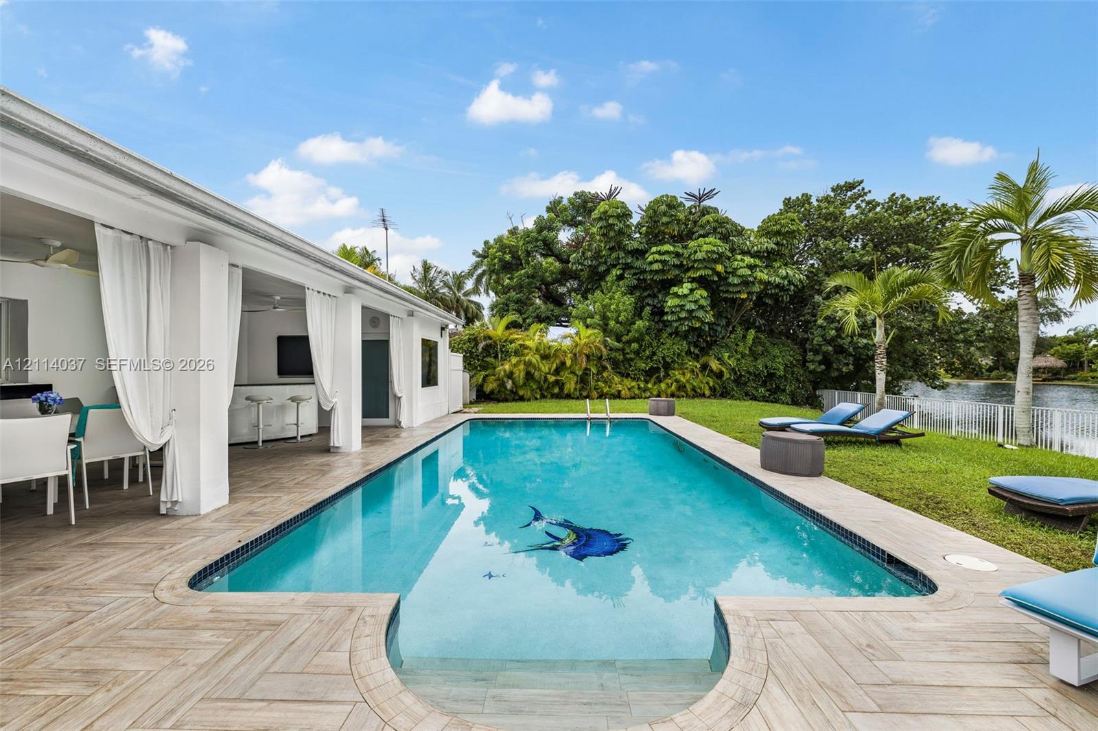 Rectangular swimming pool featuring a decorative floor inlay, bordered by herringbone-patterned tile decking and a covered outdoor patio with structural columns
