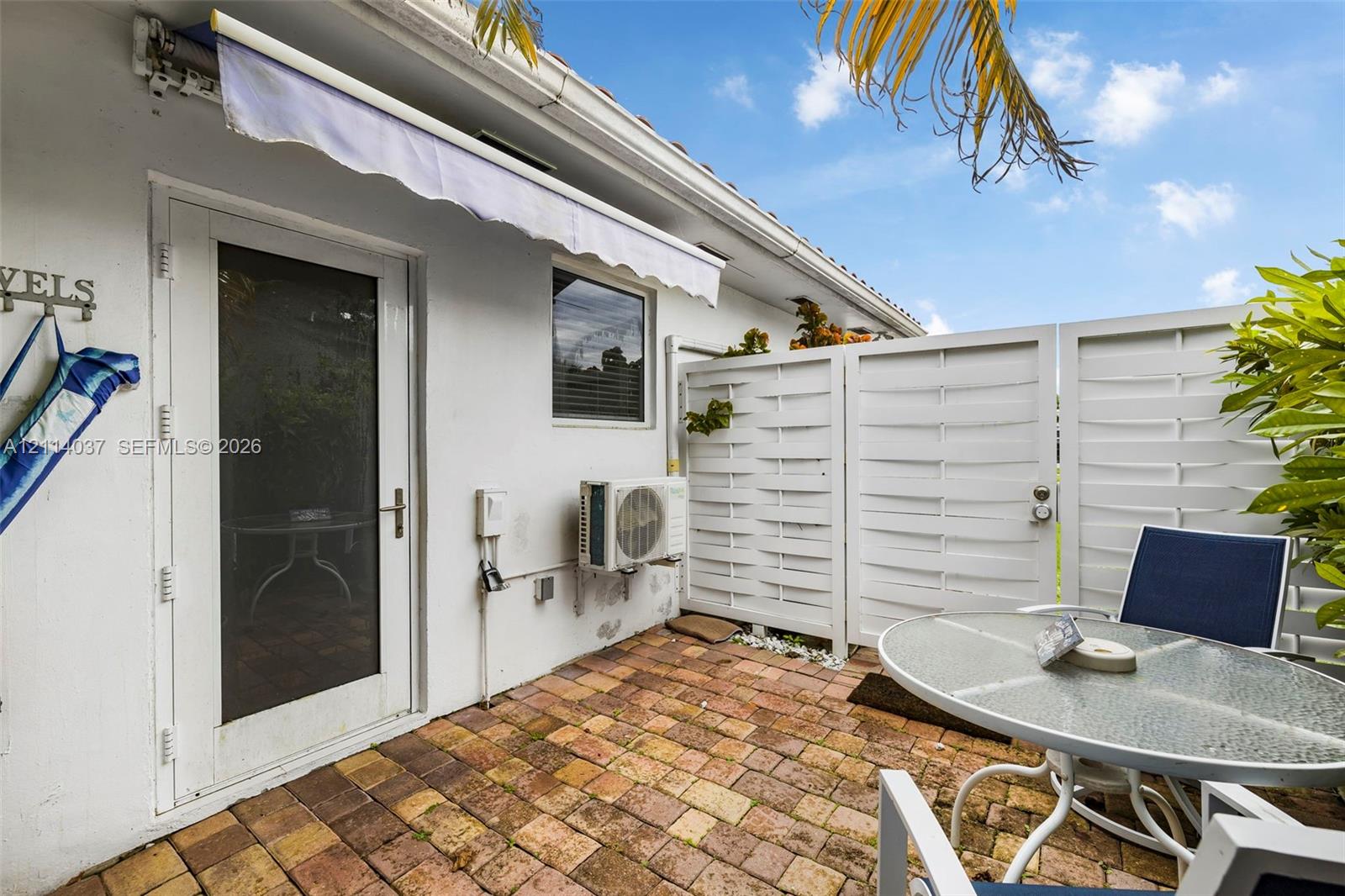 Private patio featuring brick pavers, a retractable exterior awning, and horizontal-slat privacy fencing